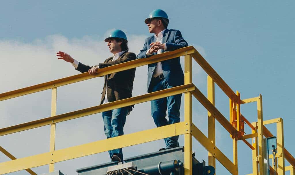 Two men standing on top of tower wearing hard hats